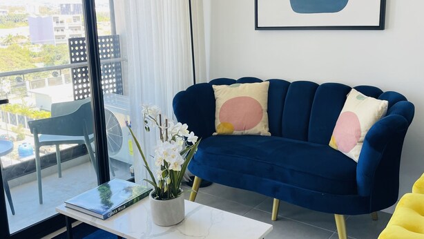 A modern living room with a dark blue sofa, a white coffee table, and a potted orchid plant.