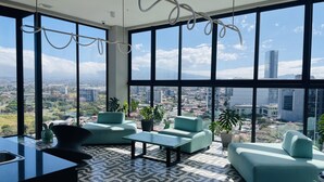 A modern living room with large windows, teal sofas, a patterned floor, and a view of a cityscape.