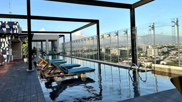 Piscina infinita en la azotea con sillones de descanso, vistas despejadas de la ciudad y un diseño arquitectónico moderno.