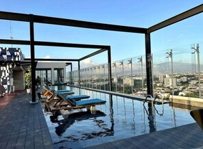A rooftop infinity pool with lounge chairs, clear views of the city, and a modern architectural design.