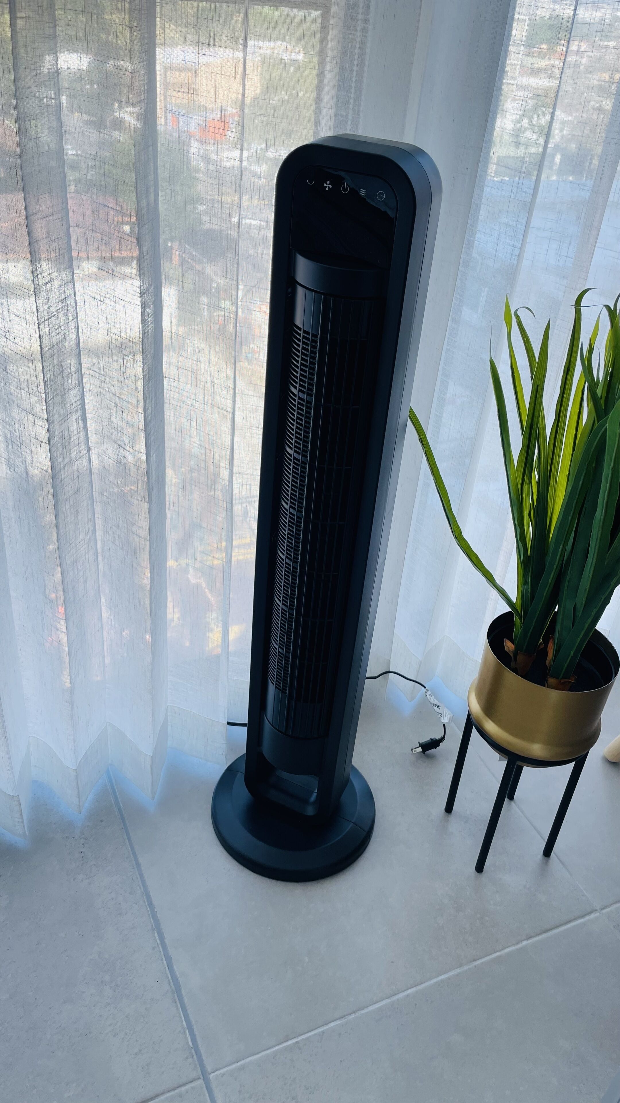 Um ventilador de chão em um quarto com vista através de cortinas finas.