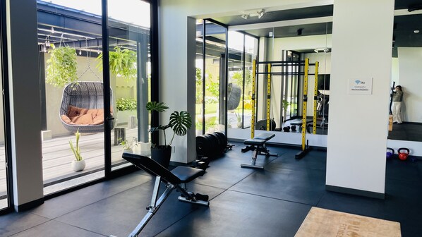 A modern gym with exercise equipment, large windows, and indoor plants.