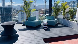A rooftop terrace with modern seating, potted plants, and a city view.