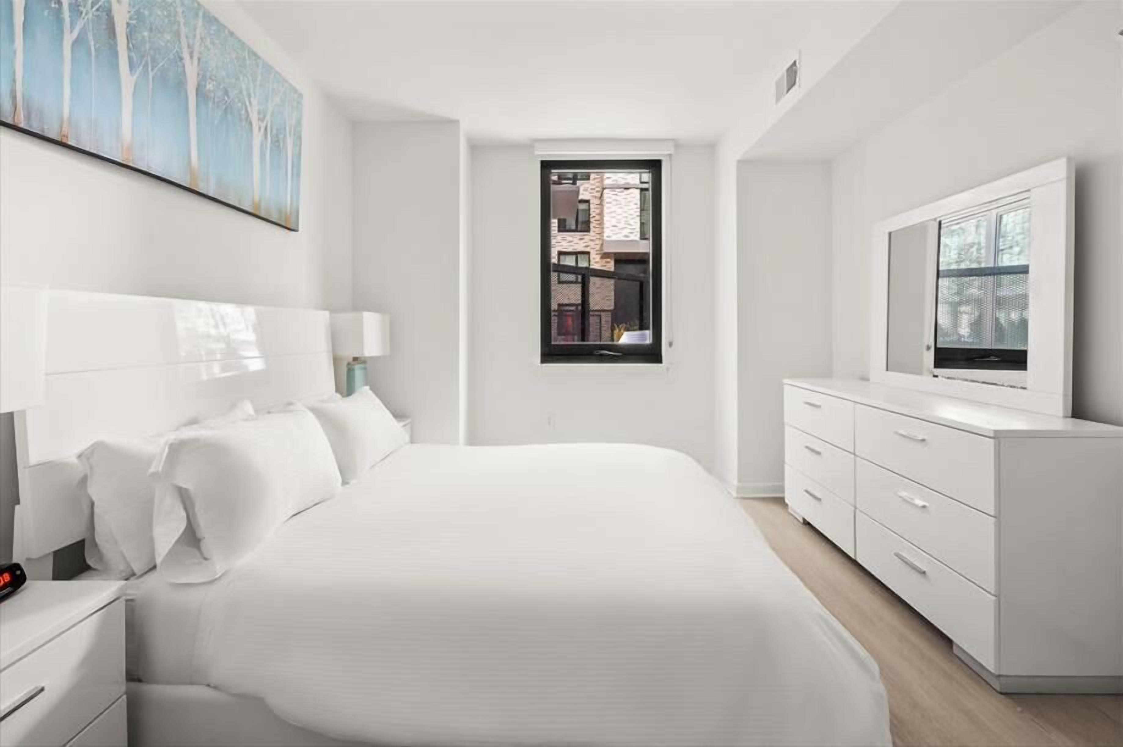 A modern bedroom with a large bed, a TV, a window, and a painting on the wall.