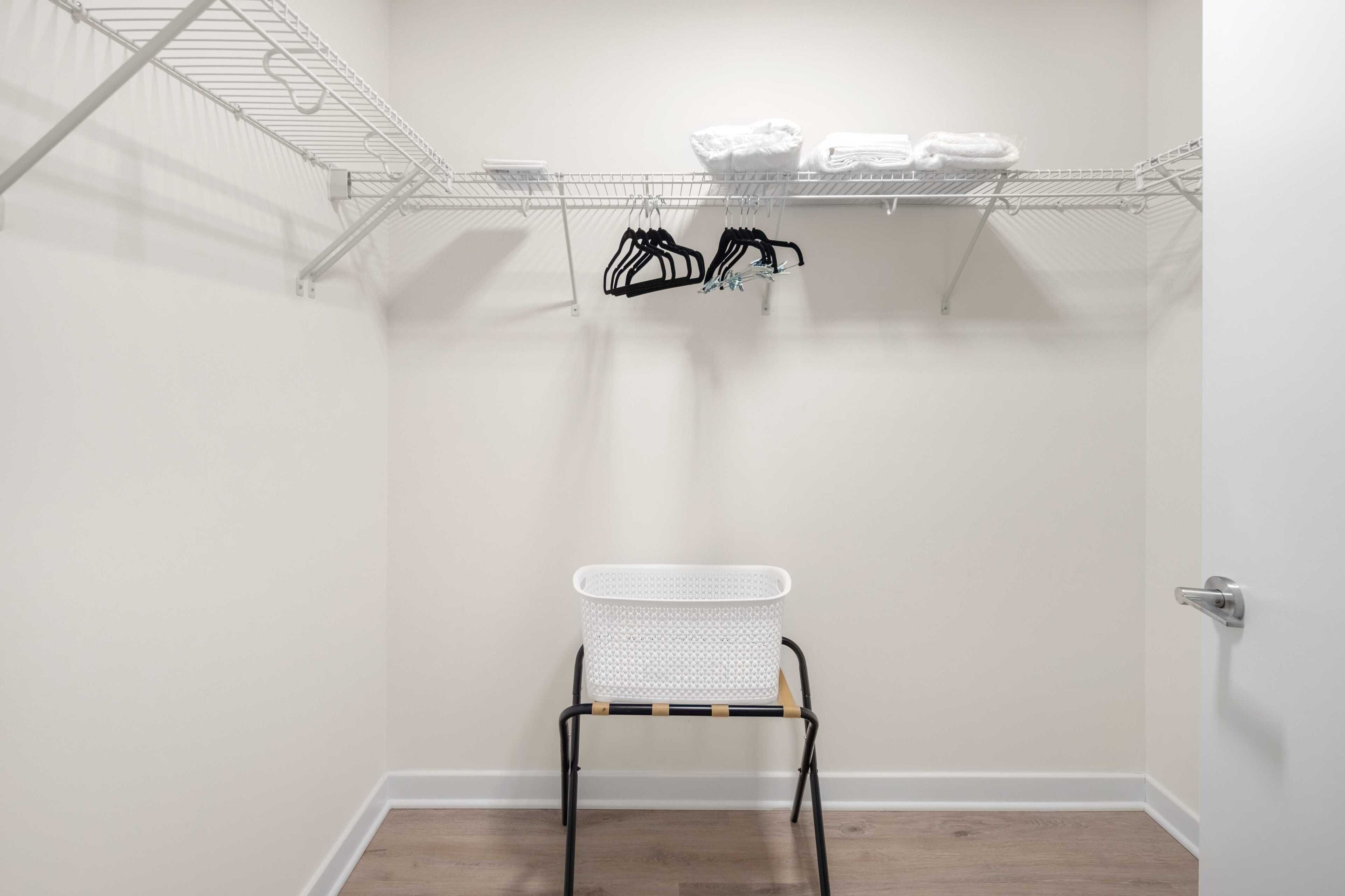 A laundry room with a metal rack, a white basket, and a shelf with folded towels.