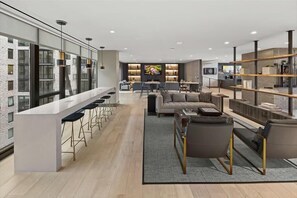 A modern kitchen with a bar area, a seating area with a sofa and chairs, and a large TV screen.