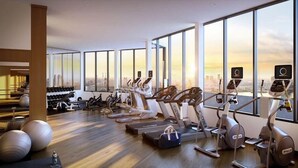 Un gimnasio moderno con varios equipos de ejercicio, ventanas amplias y vistas a la ciudad.