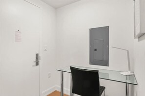 A room with a glass desk, a black chair, a door with a lock, and a wall-mounted light fixture. - Short Walk to Park Ave 1BR | near Grand Central (New York)