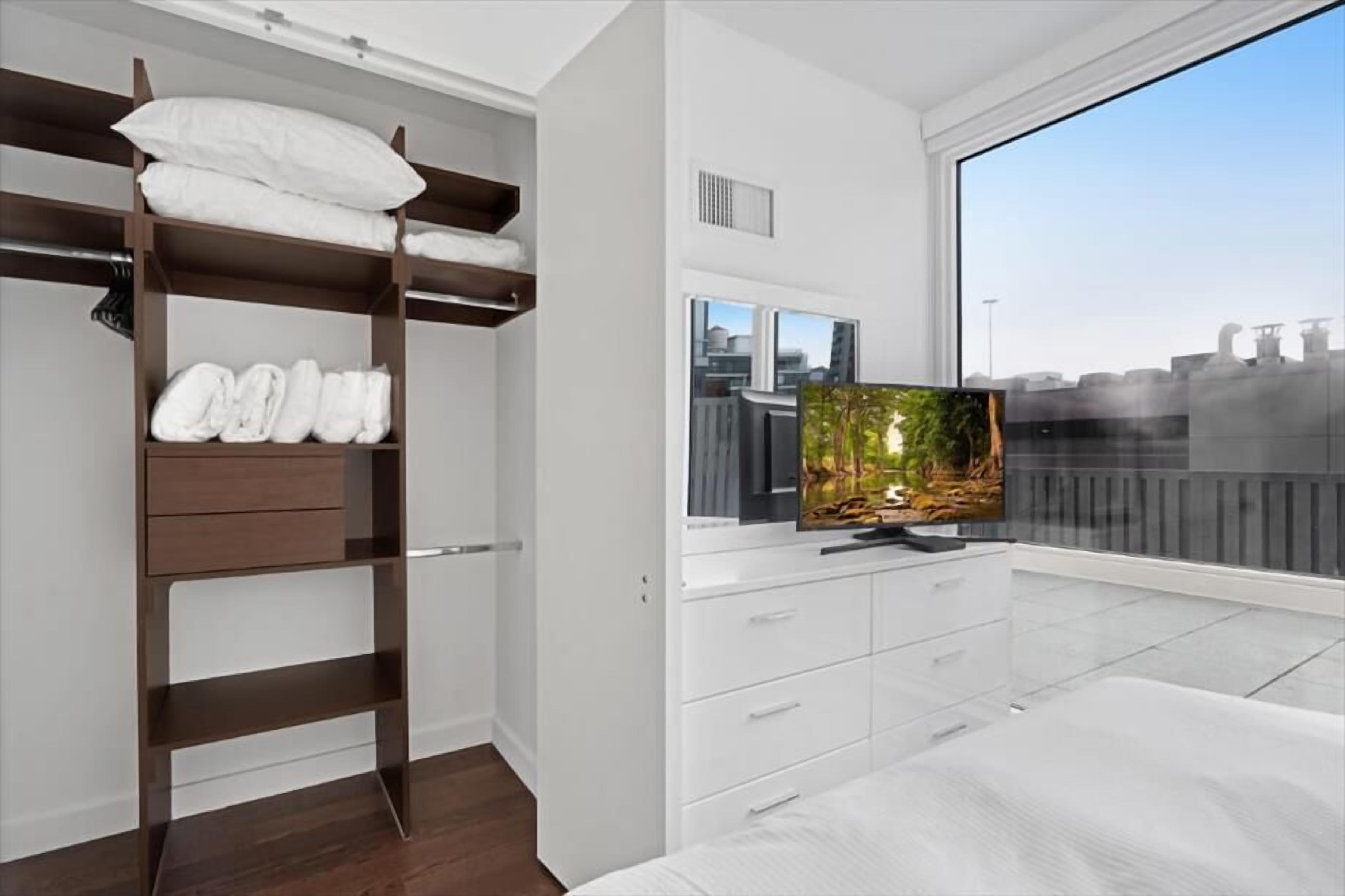 Une chambre moderne avec un lit superposé, une grande fenêtre donnant sur la ville et un téléviseur à écran plat posé sur une commode blanche.