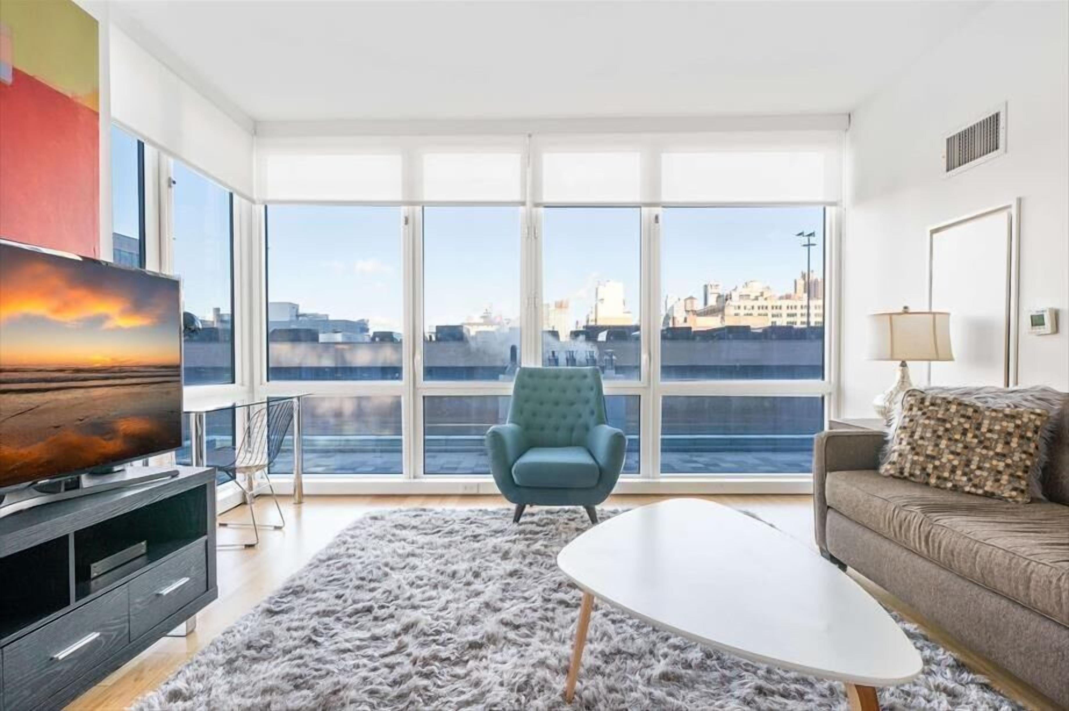 Ein modernes Wohnzimmer mit großem Fenster, einer Couch, einem Couchtisch und einem Fernseher.