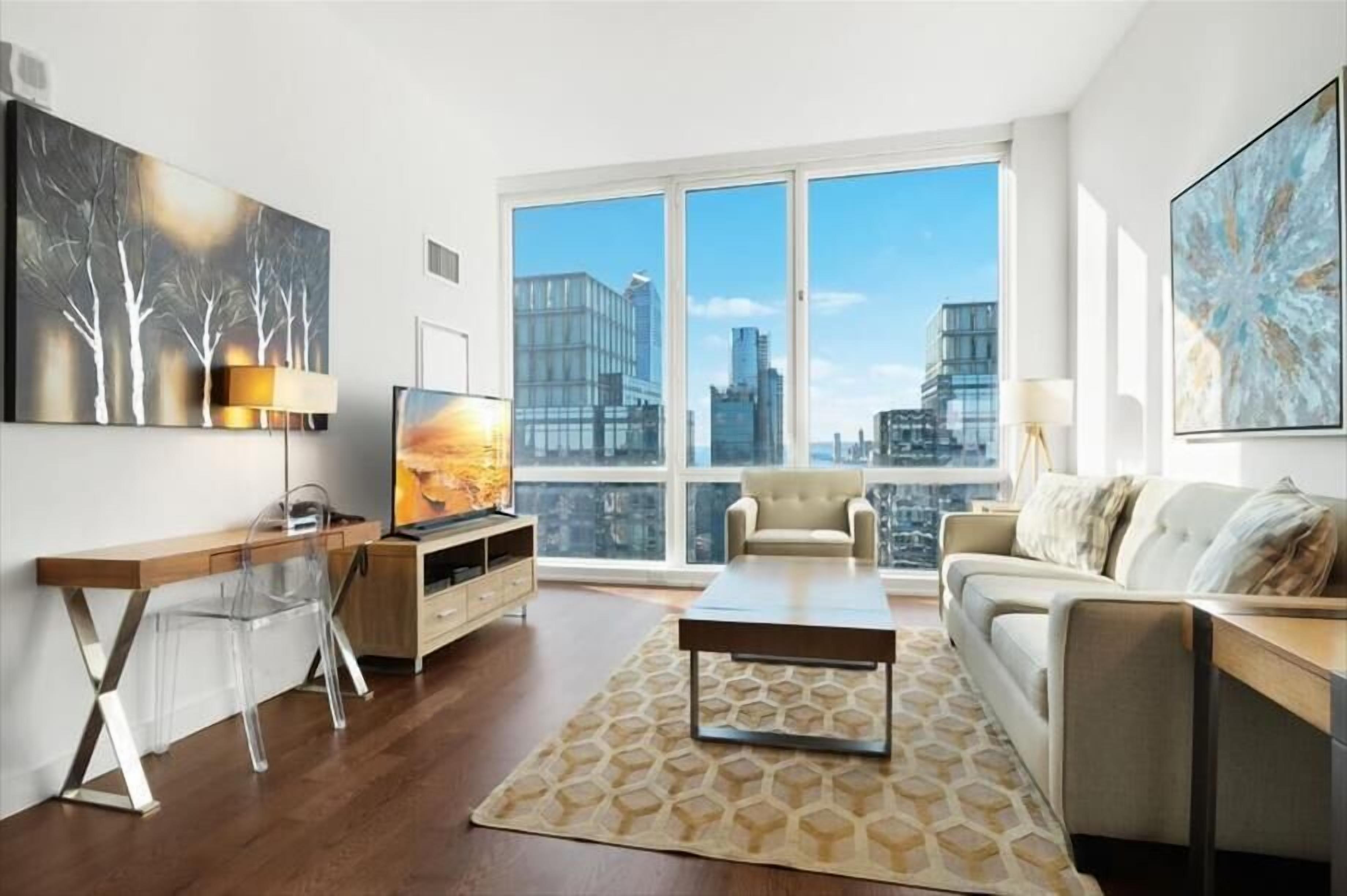 A modern living room with a large window, a sofa, a coffee table, and a TV.