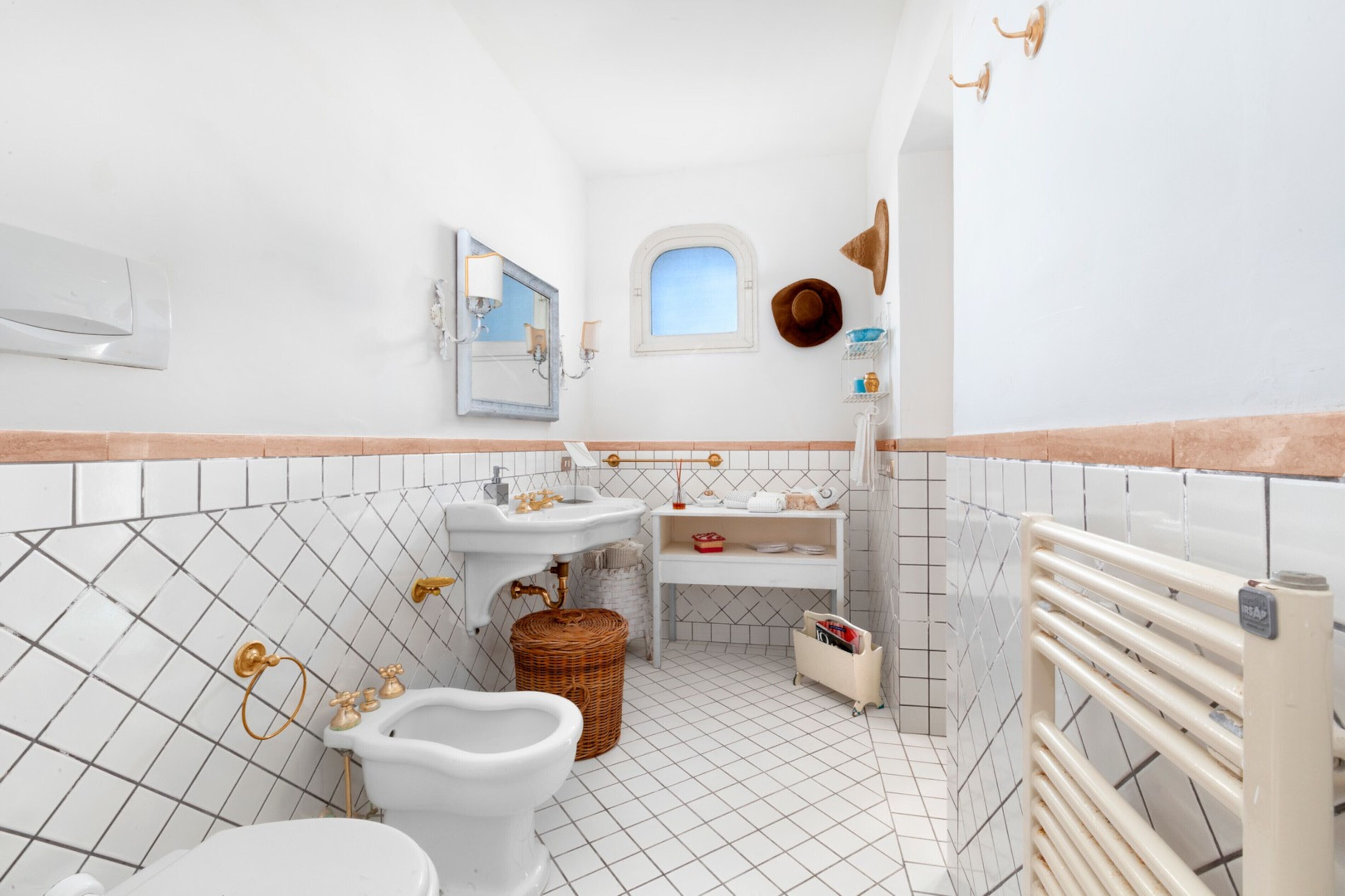 A bathroom with white tiled walls, a white sink, a white toilet, a wicker basket, and a towel rack.