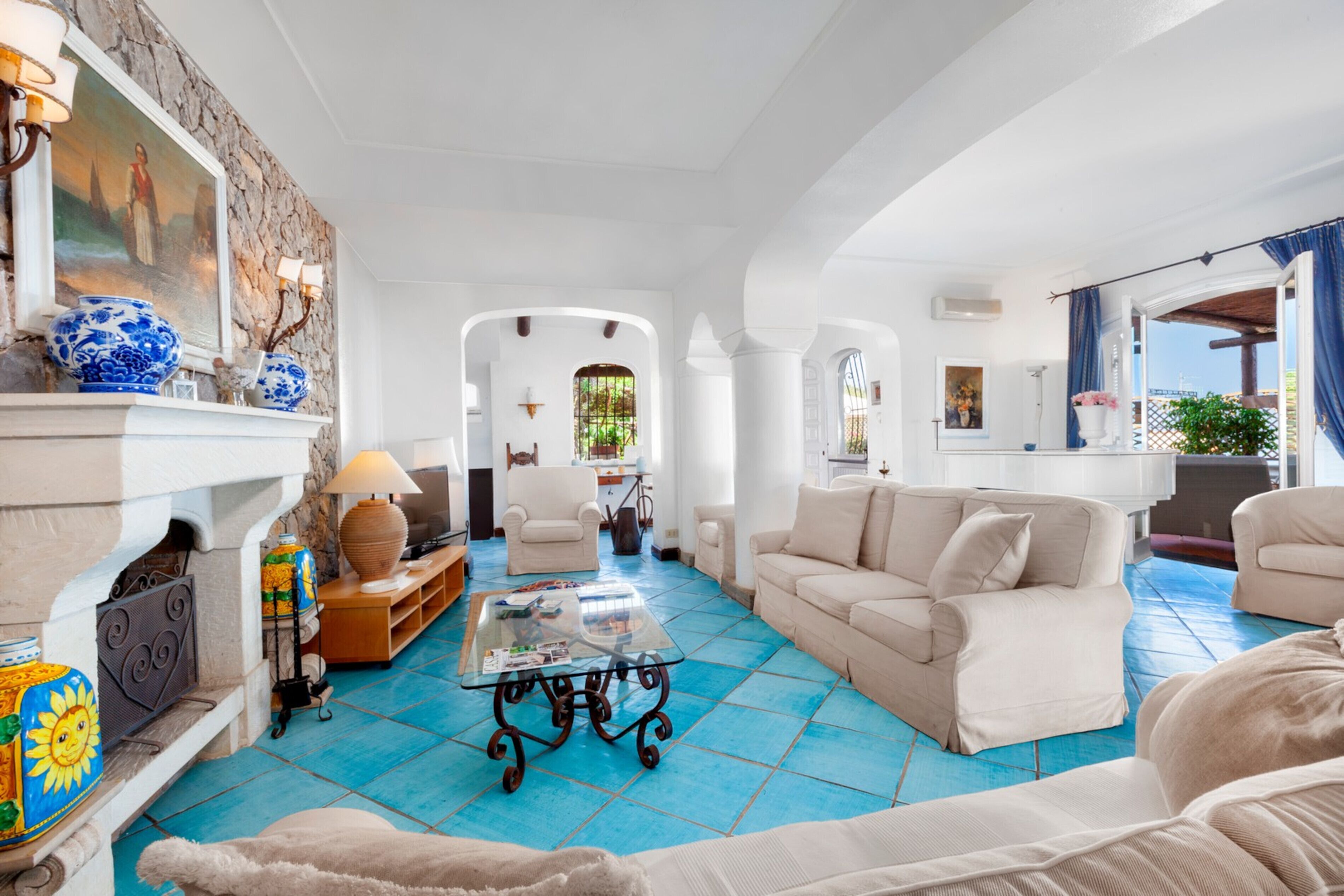 A spacious living room with a fireplace, a coffee table, and a sofa. There is a view of the outside through an open archway.