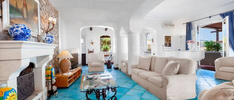 A spacious living room with a fireplace, a coffee table, and a sofa. There is a view of the outside through an open archway.