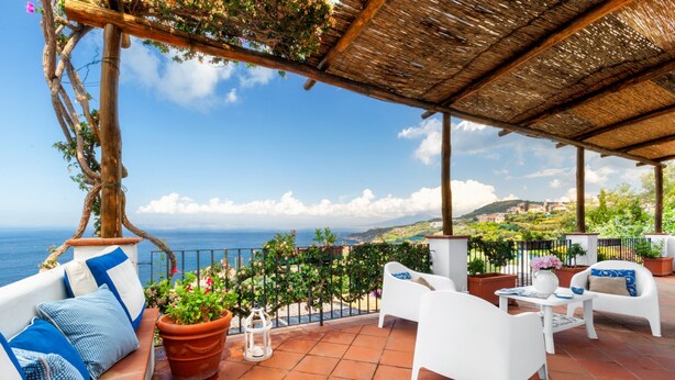 A terrace with white furniture, potted plants, and a view of the sea. - YourHome - Villa Mia (Massa Lubrense)
