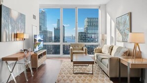 A modern living room with a city view, a sofa, a coffee table, and a desk with a chair.