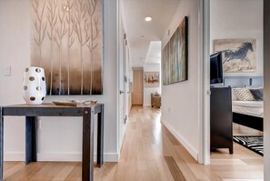 A modern interior with a wooden floor, a dining area with a table and chairs, a hallway leading to a bedroom with a bed and a TV. - Steps from Hudson River 1 Deluxe BR city view | Huge Windows (New York)