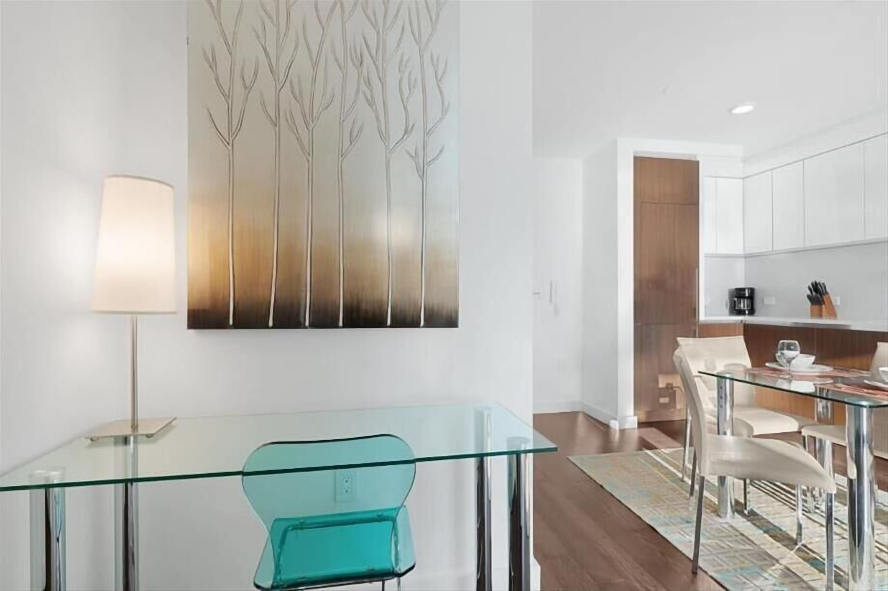 Une cuisine moderne avec des meubles blancs, une table à manger en verre et une chaise de couleur turquoise.