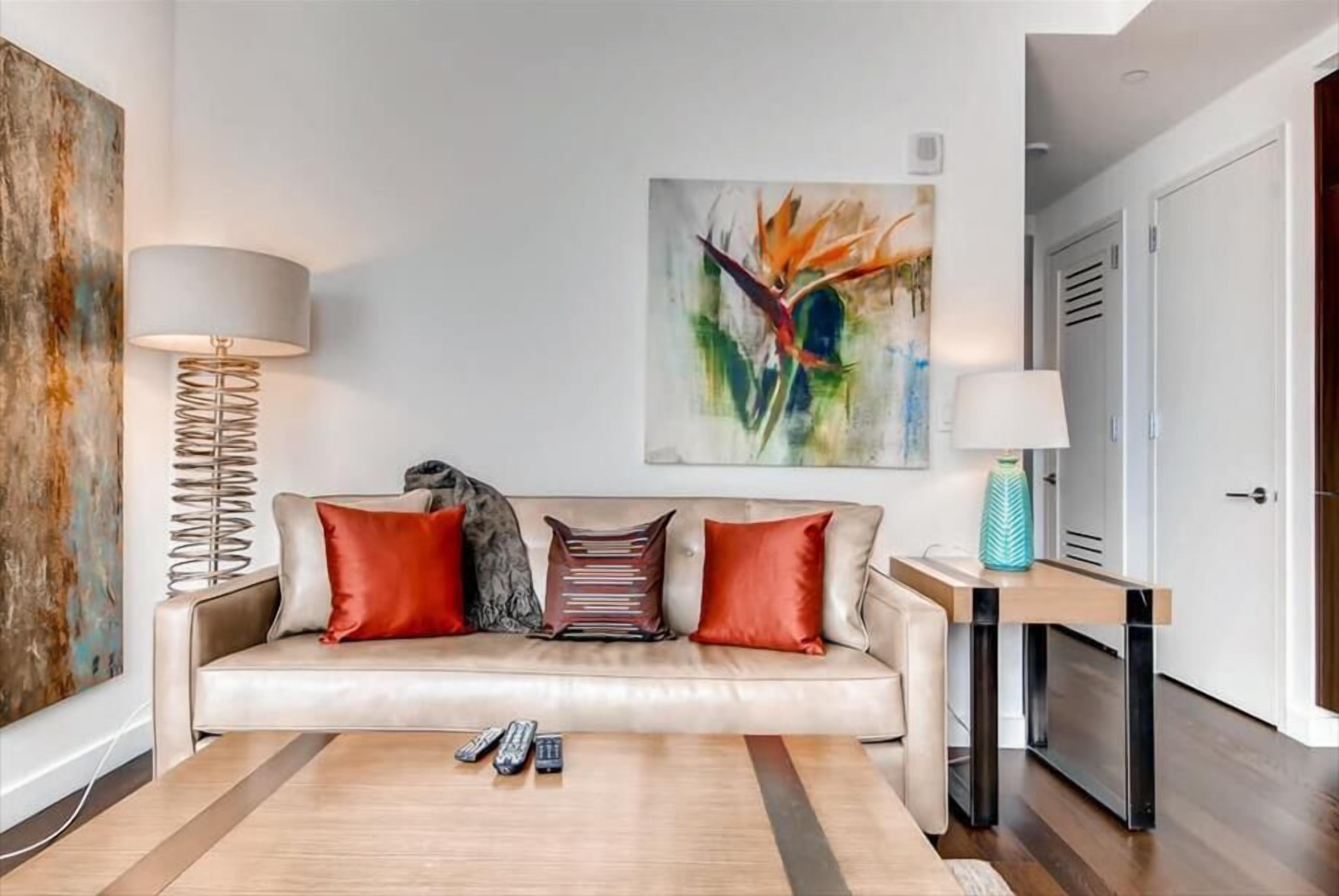 Un salon moderne avec un canapé, deux coussins rouges, une table basse et un tableau accroché au mur.