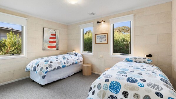 Ein Schlafzimmer mit zwei Einzelbetten, einem kleinen Nachttisch, einem an der Wand befestigten Regal und einem Fenster mit Blick ins Grüne.