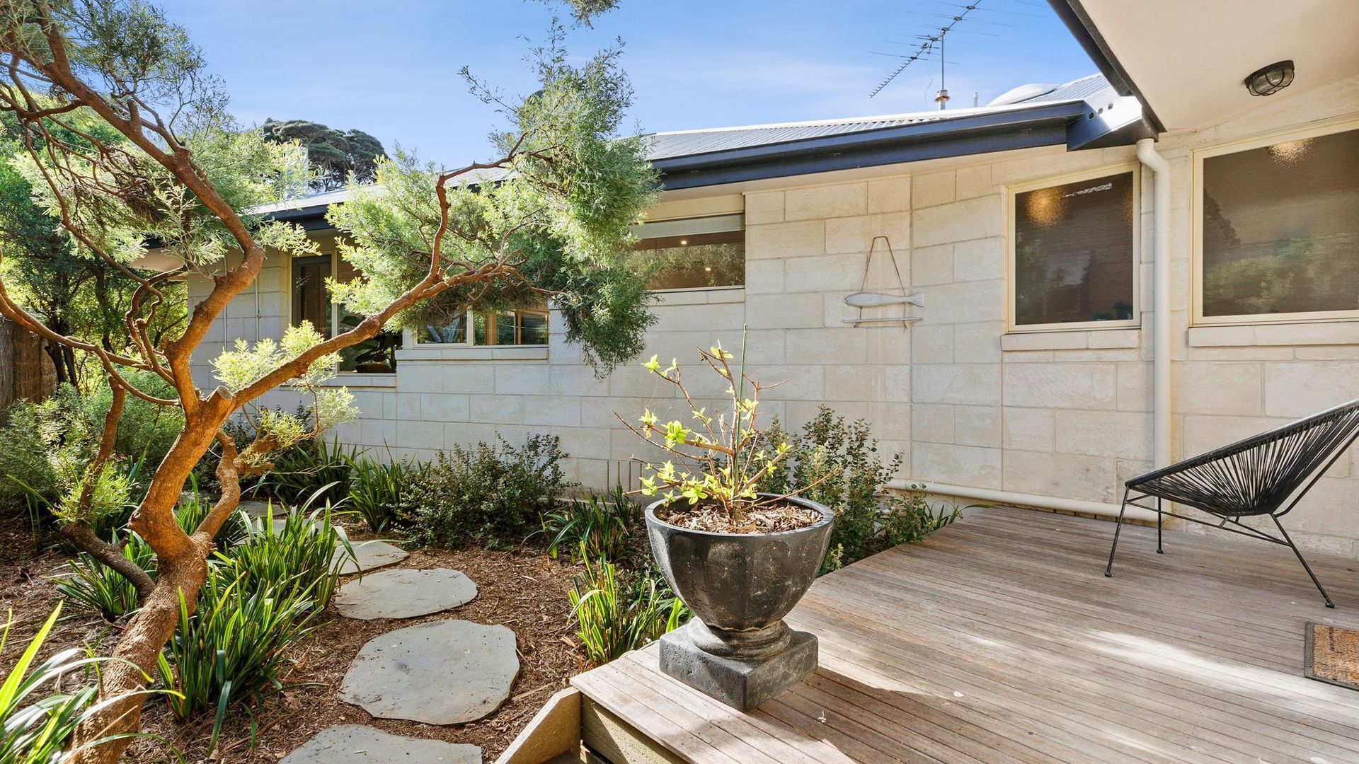 A modern house with a wooden deck, stone pathway, and a potted plant.