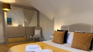 Habitación de hotel con una cama grande, dos almohadas, una silla, una lámpara y vistas al exterior.