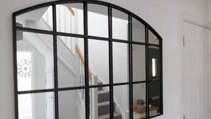 Un espejo grande de marco negro con un patrón de cuadrícula, que refleja una escalera y un reloj.