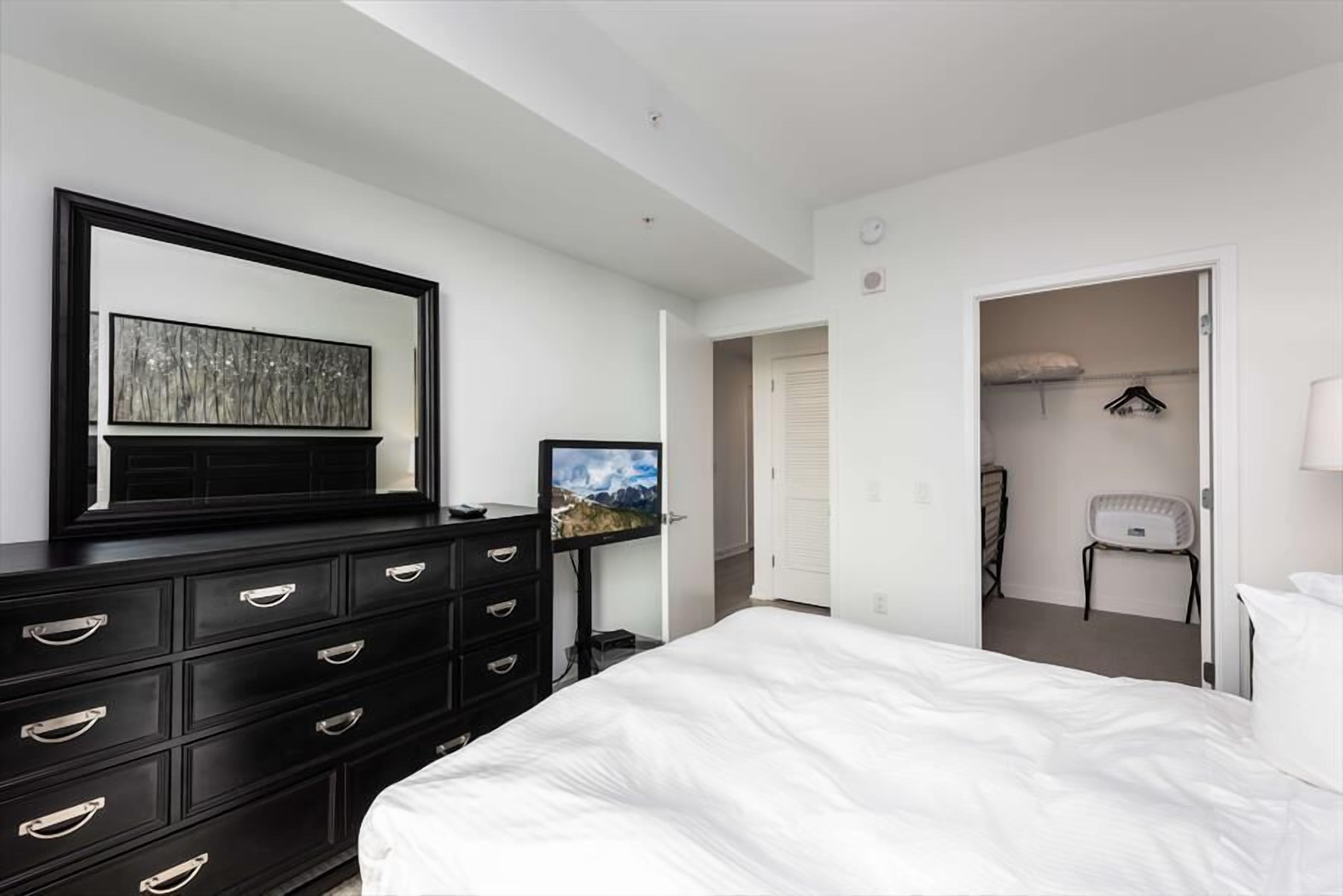 Ein Schlafzimmer mit einem großen Bett, einer Kommode mit Schubladen, einem Flachbildfernseher und einer Tür zu einem Badezimmer.