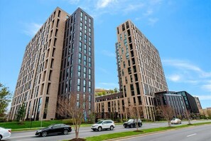 Two tall, modern buildings with a grid-like facade, a well-maintained road with parked cars, and a clear blue sky.