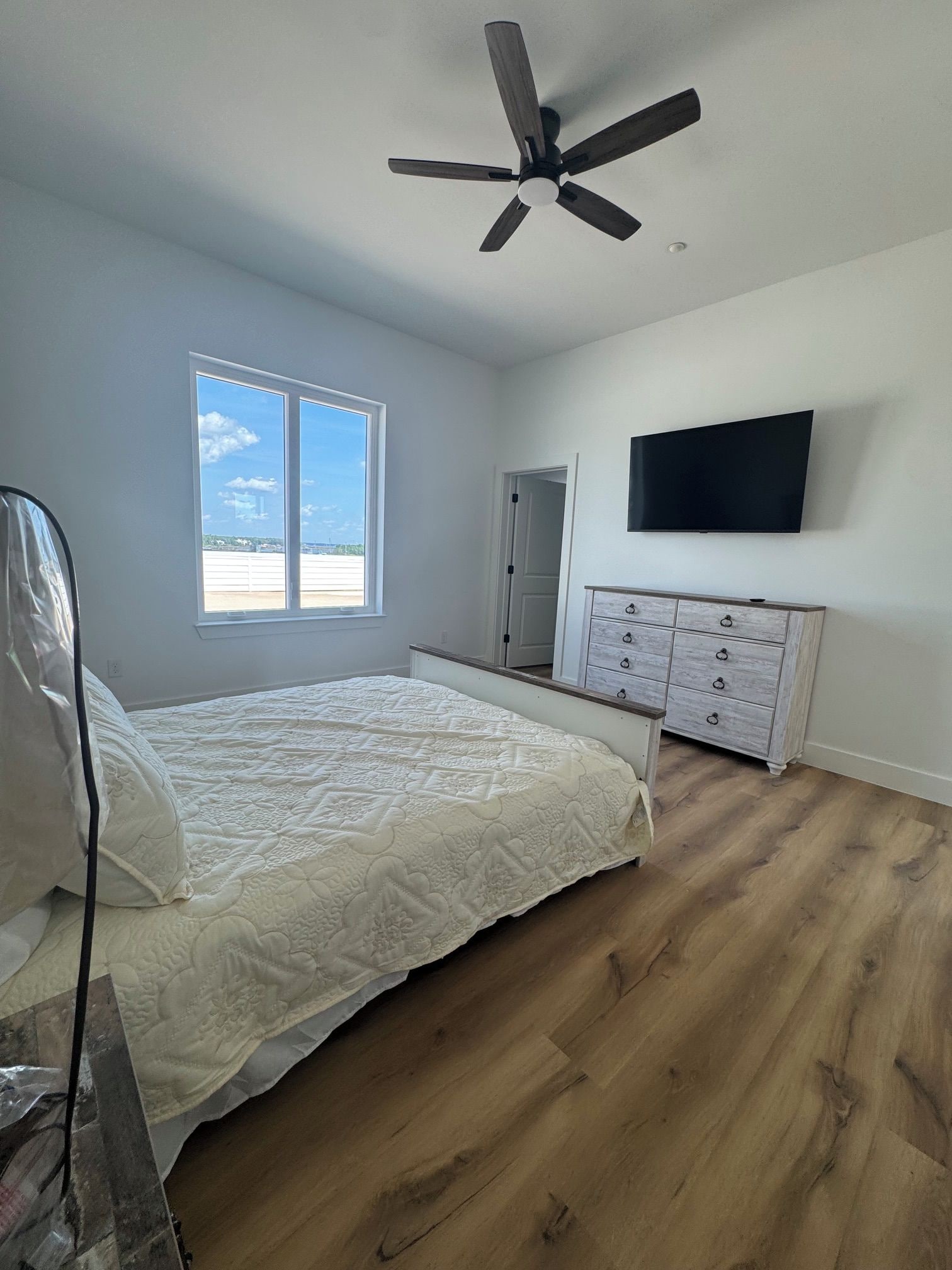 Une chambre à coucher avec un lit, un ventilateur de plafond, une commode, un téléviseur et une fenêtre donnant sur un beau paysage.