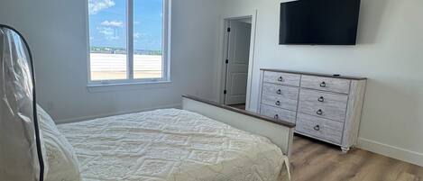 Un dormitorio con cama, ventilador de techo, cómoda, televisor y ventana con vista.
