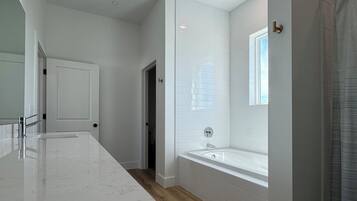 A modern bathroom with a large mirror, a bathtub, and a shower area.