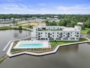 A modern building with a swimming pool, surrounded by water and greenery. - Handsboro Pointe Condo & Suites (Gulfport)