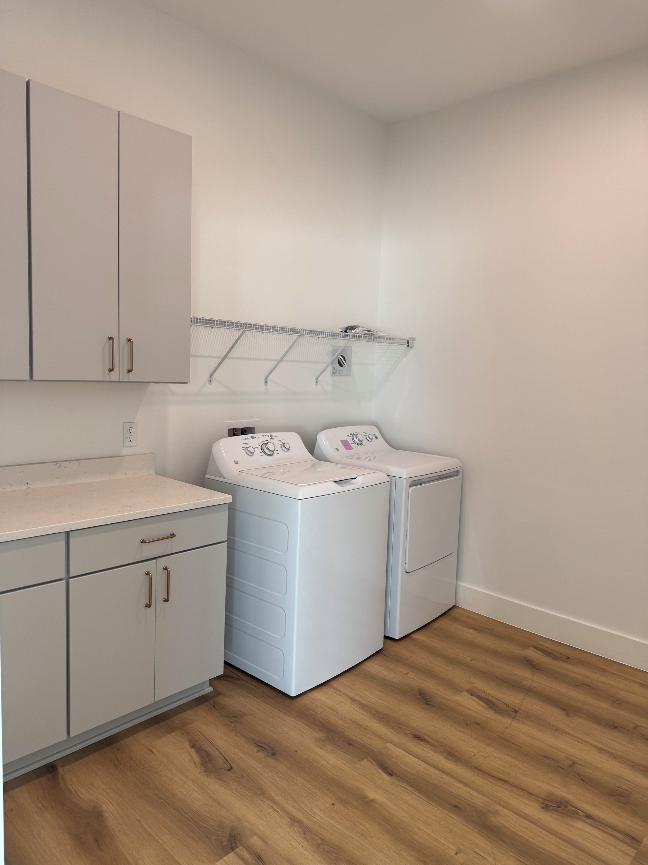 A laundry room with two white washing machines, a metal drying rack, and grey cabinets with handles.
