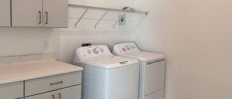 A laundry room with two white washing machines, a metal drying rack, and grey cabinets with handles.