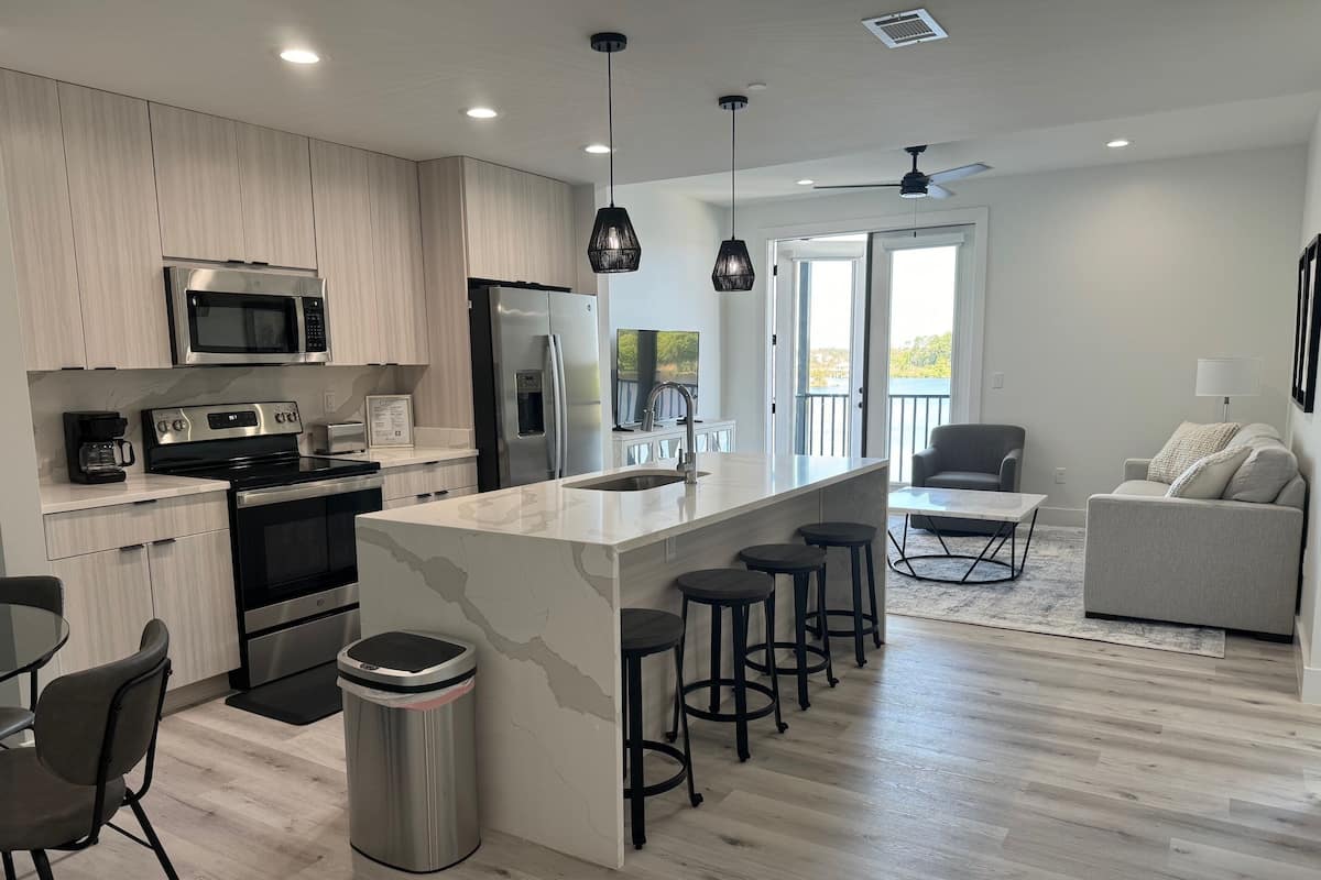 A modern kitchen with a central island, stainless steel appliances, and a view to the outside.