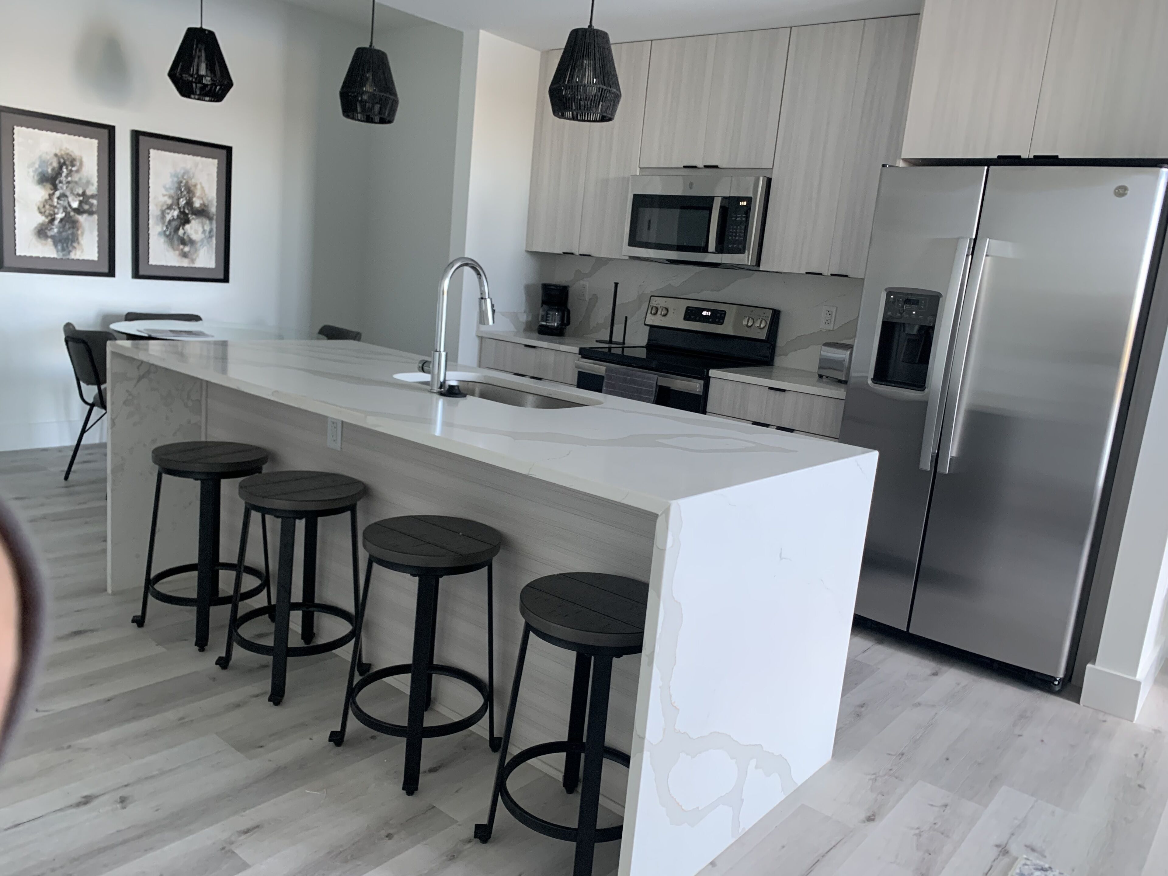 A modern kitchen with a large island, stainless steel appliances, and black bar stools.