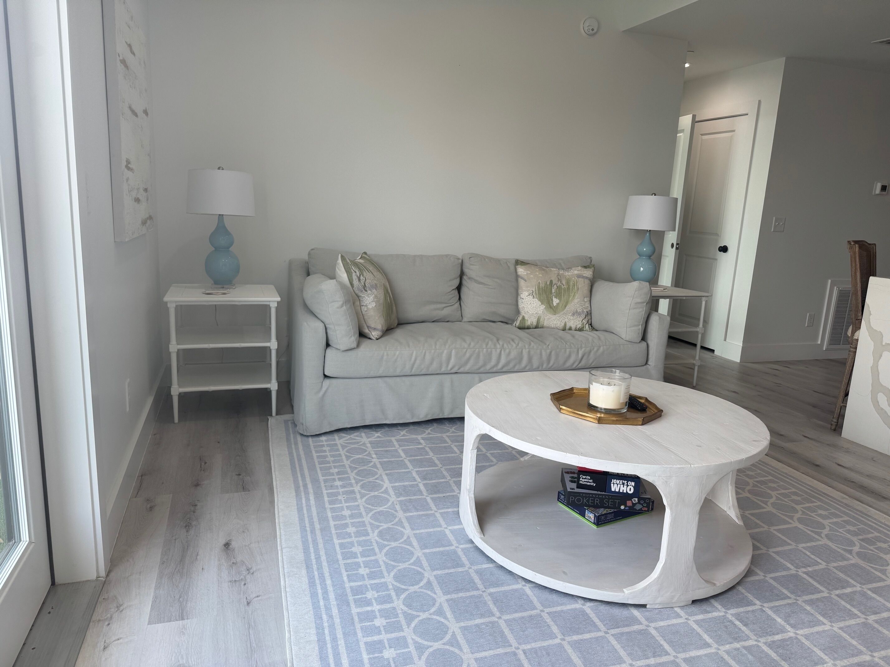 Un salon moderne avec un canapé gris, des tables d’appoint blanches et une table basse ronde sur laquelle est posé un plateau.