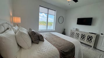A bedroom with a bed, a window with a view, a ceiling fan, a wall-mounted TV, and a radiator.