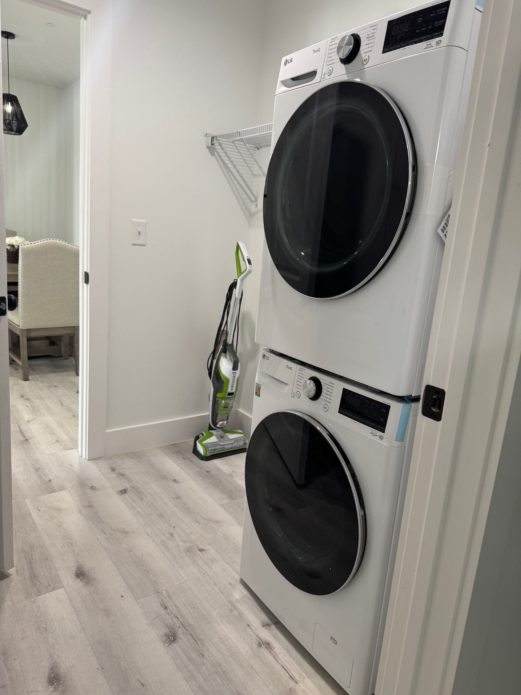 Une buanderie avec deux machines à laver à chargement frontal superposées, un aspirateur et une chaise au fond de la pièce.