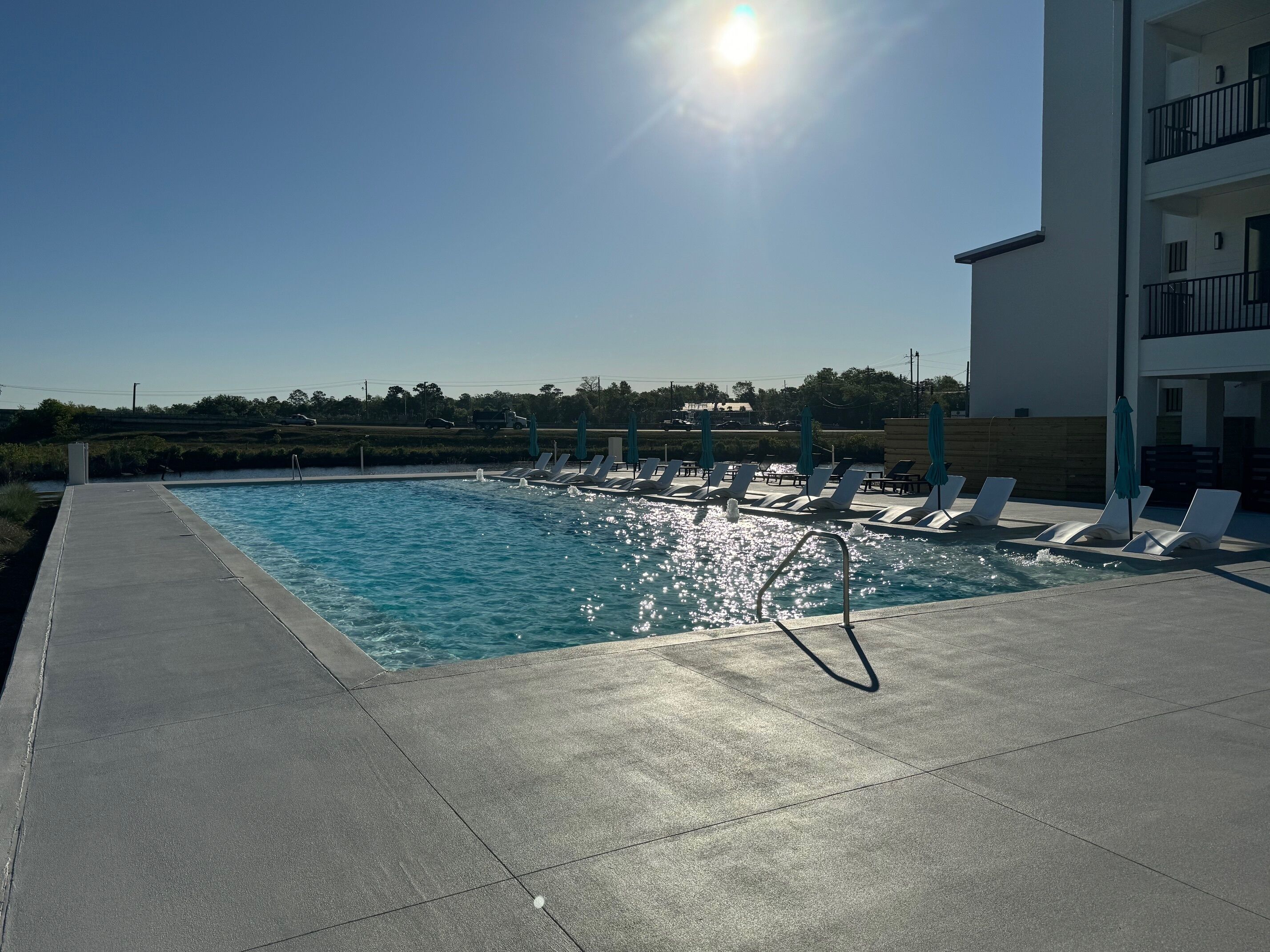 A swimming pool with sunbathing loungers and a clear sky.