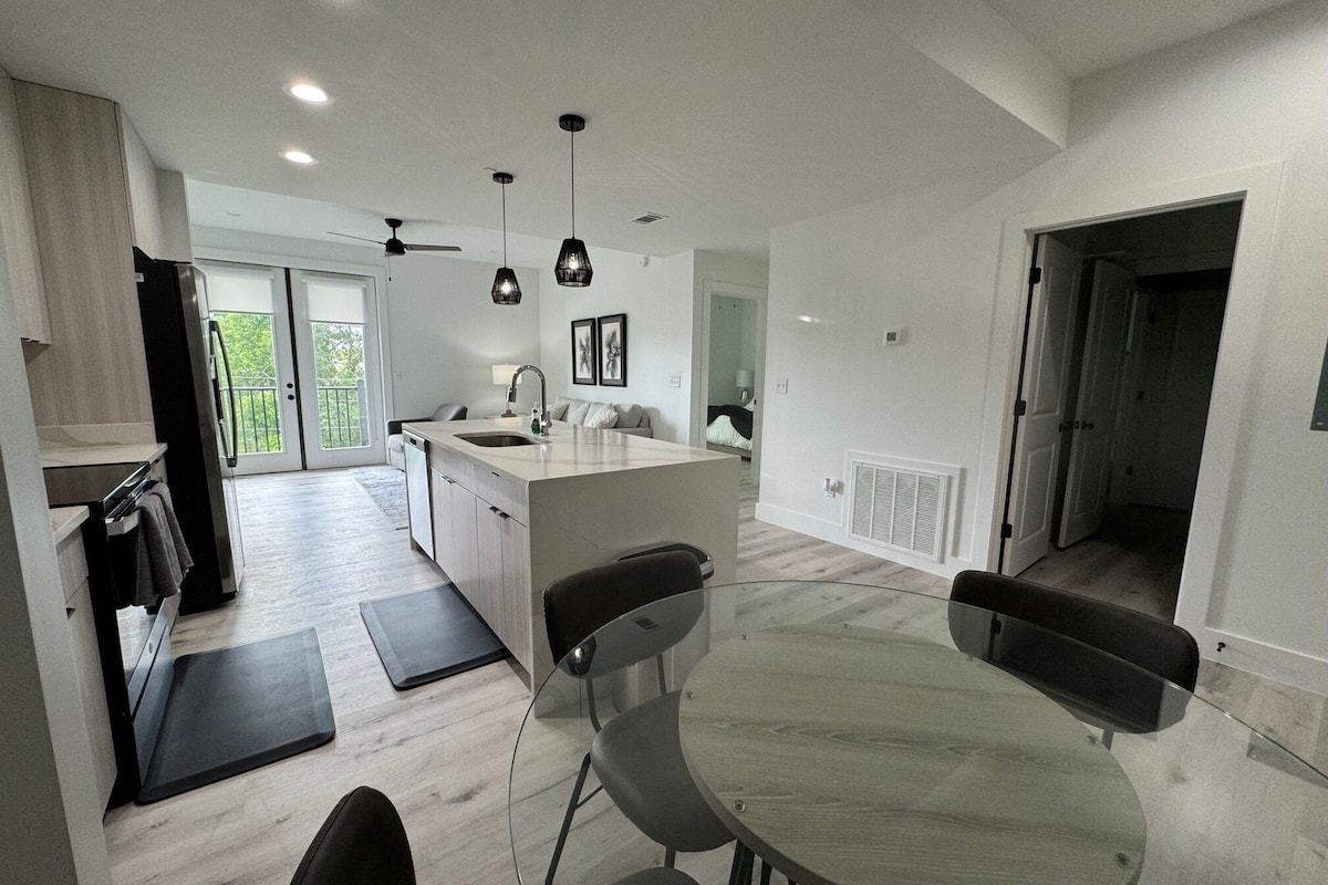 A modern kitchen with a central island, a dining area with a round table and chairs, and a ceiling fan.