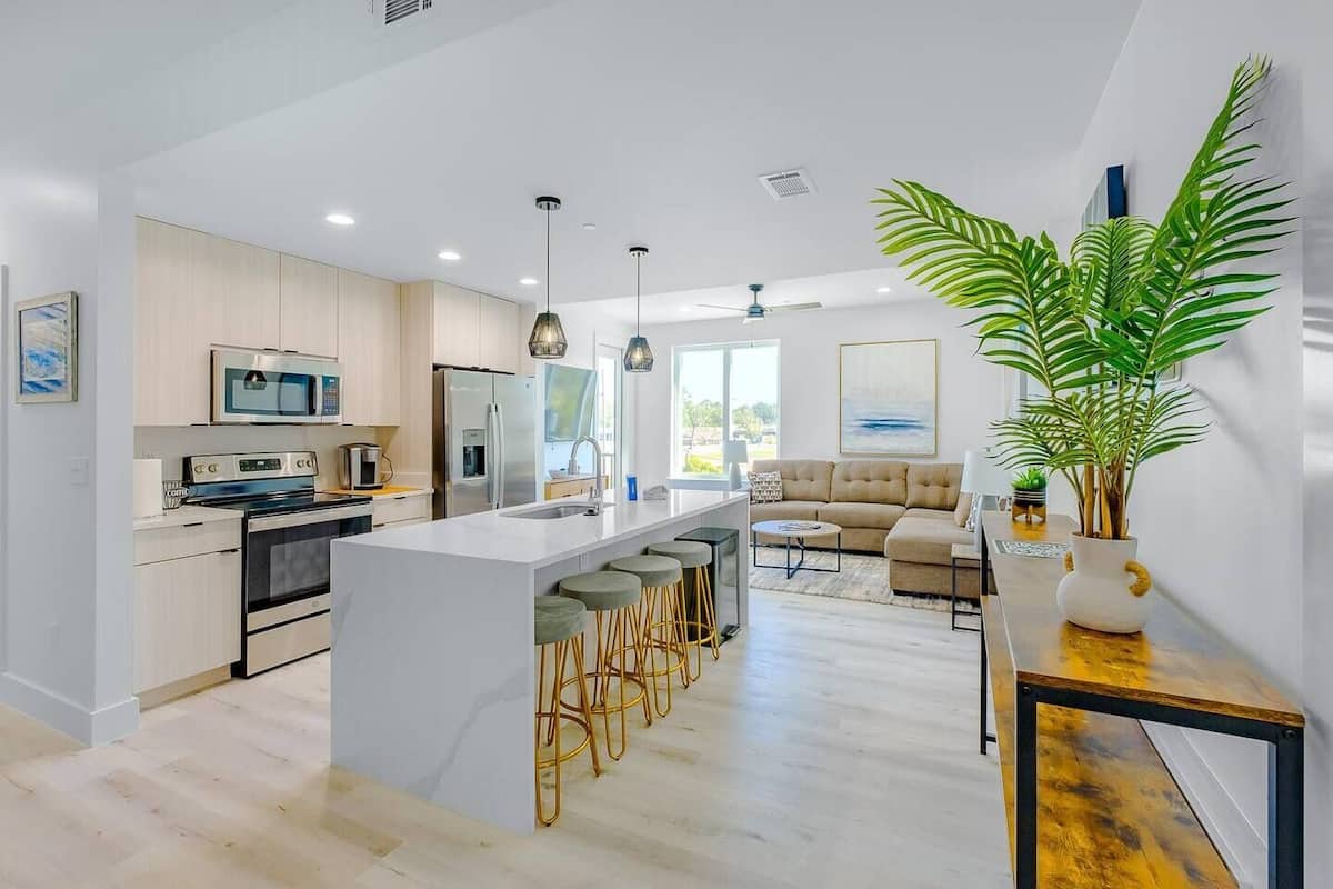 A modern kitchen with a central island, bar stools, and a dining area with a sofa.