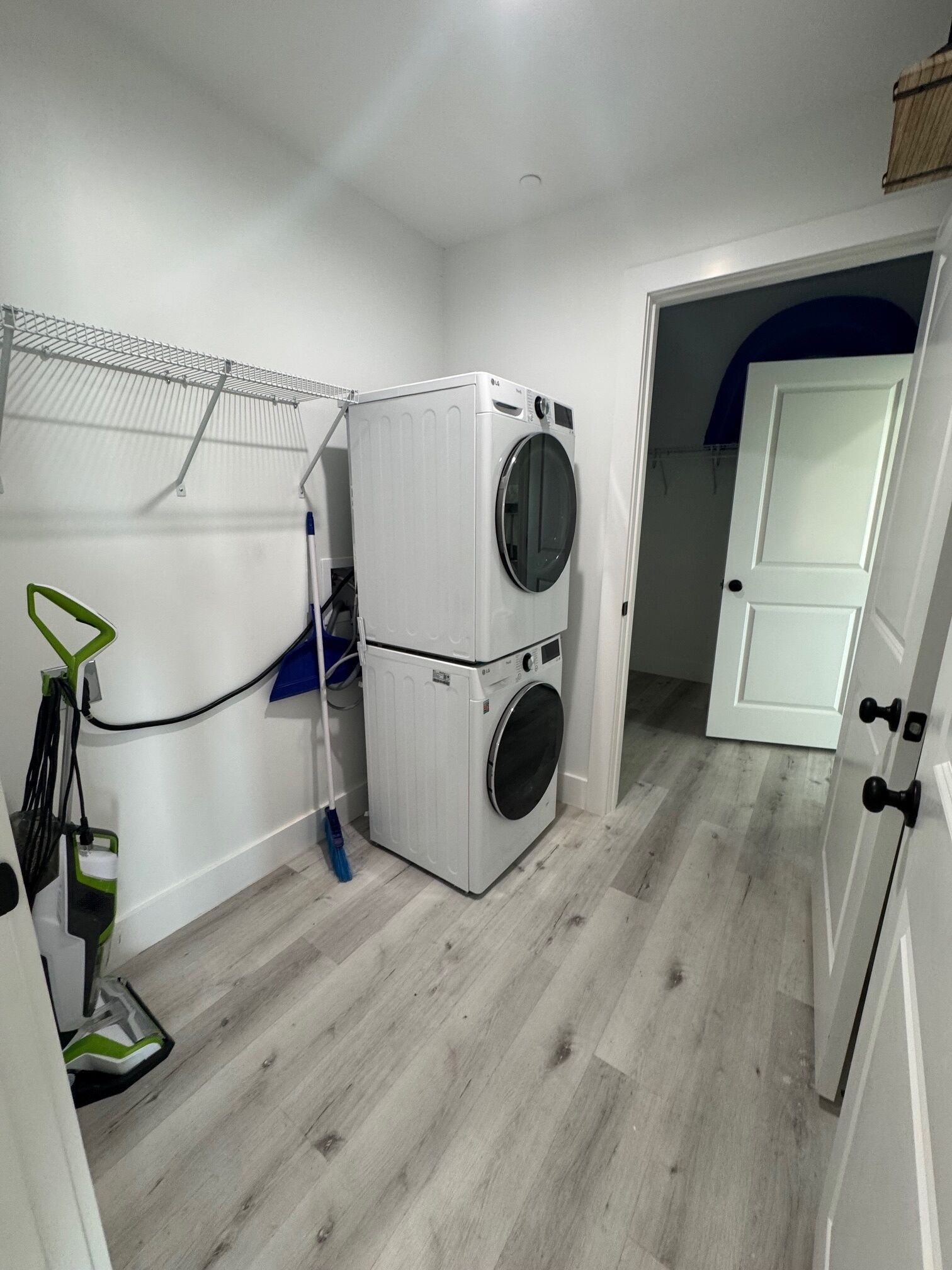 Une buanderie équipée d’un lave-linge et d’un sèche-linge superposés, d’un étendoir et d’un balai.