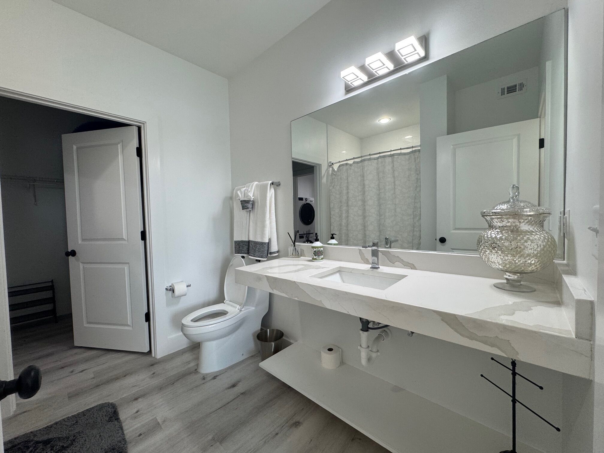 Un baño moderno con lavamanos, espejo y retrete blancos.