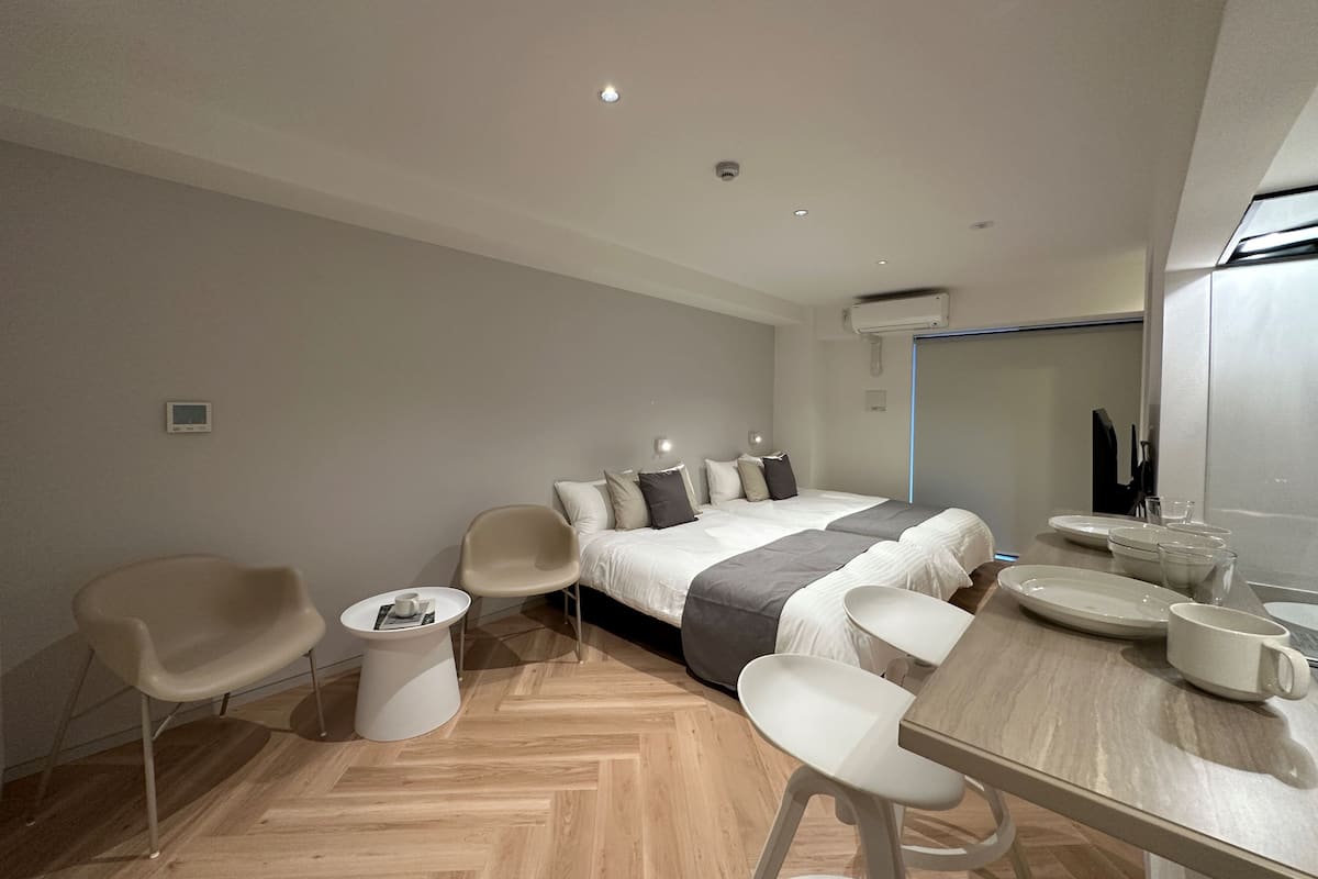 A modern hotel room with a large bed, two chairs, a small round table, and a dining table with plates and cups.