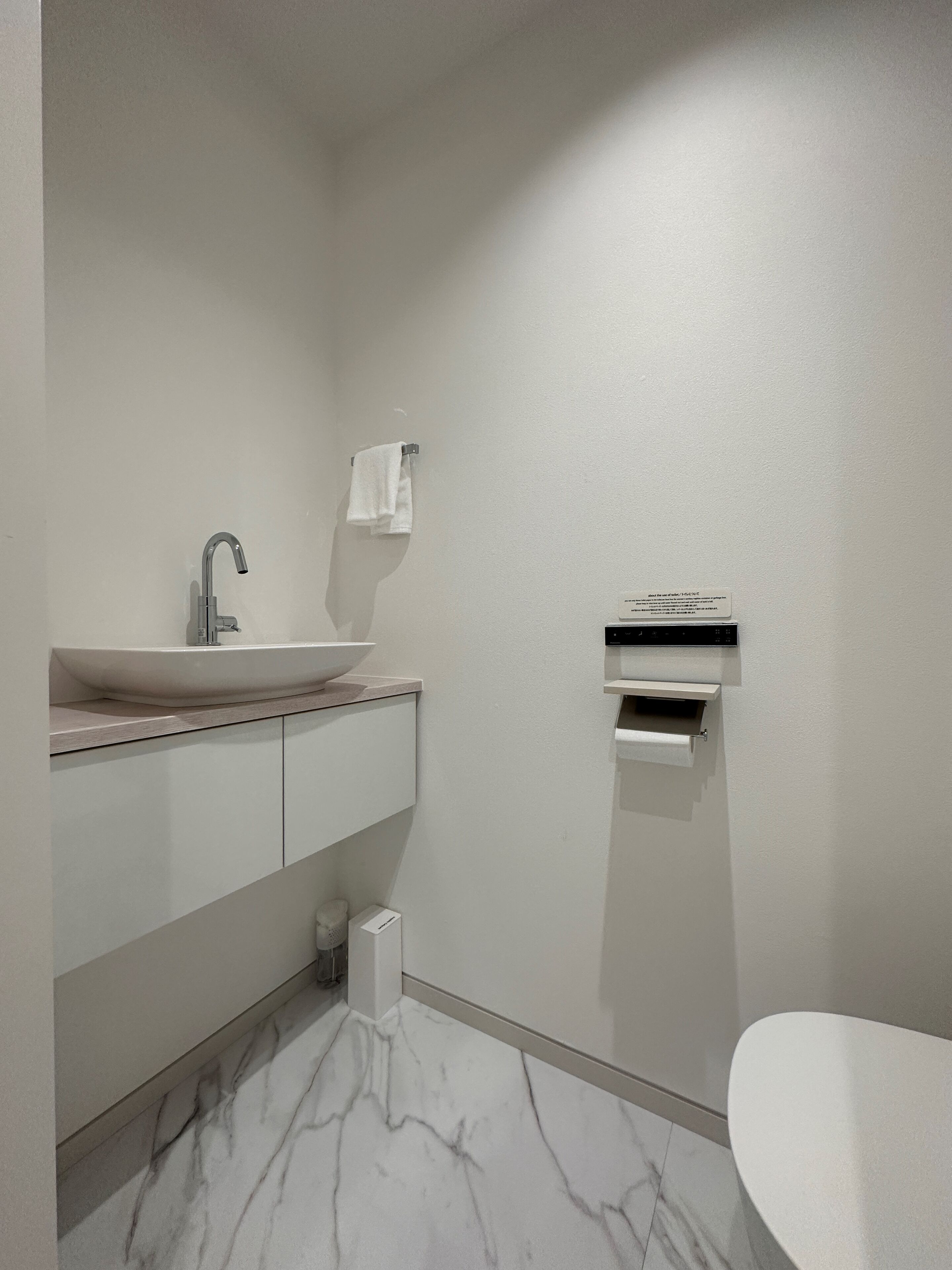 A modern bathroom with a white sink, a mirror, a towel rack, a toilet paper holder, and a marble floor.