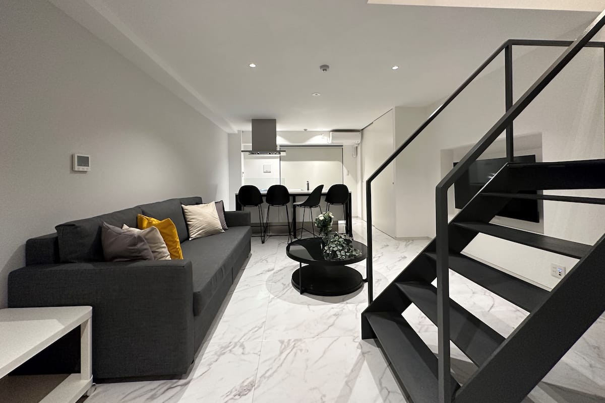 A modern living room with a grey sofa, a coffee table, and a staircase.