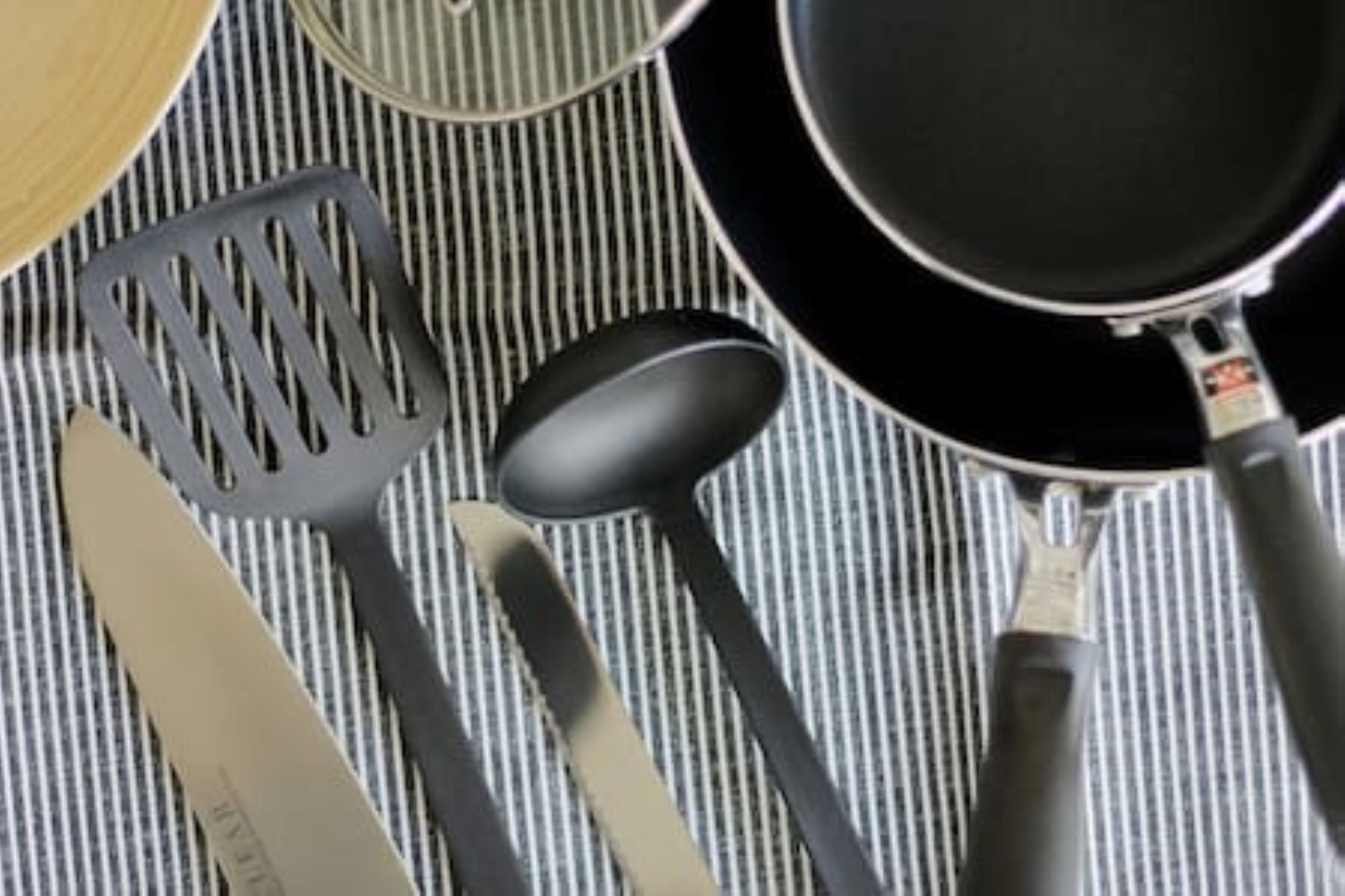 Uma cozinha com bancada listrada, uma frigideira preta, uma espátula, uma colher e uma faca.