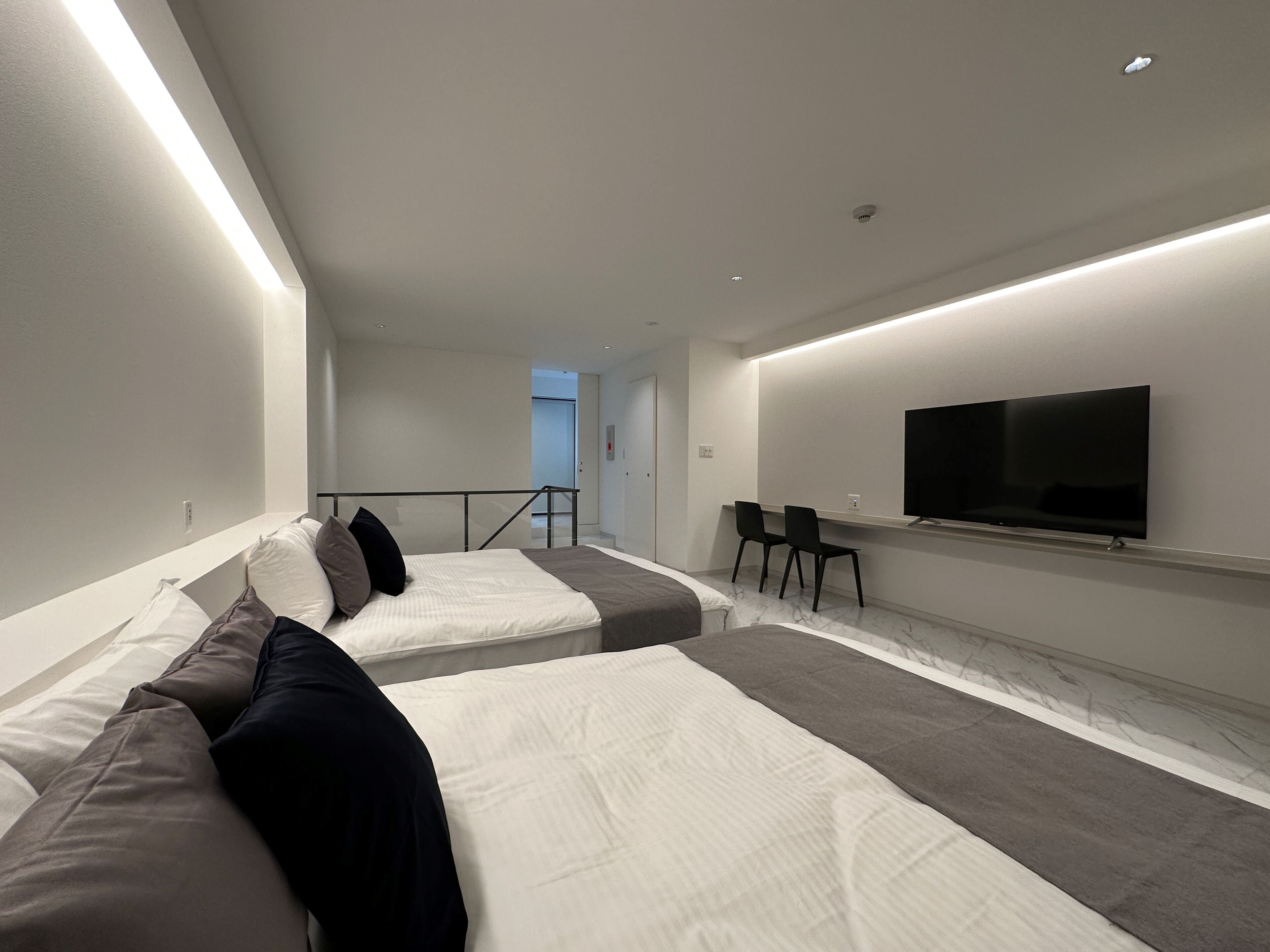 Ein modernes Hotelzimmer mit einem großen Bett, einem kleineren Bett, einem Fernseher und einer Sitzecke mit Sesseln.